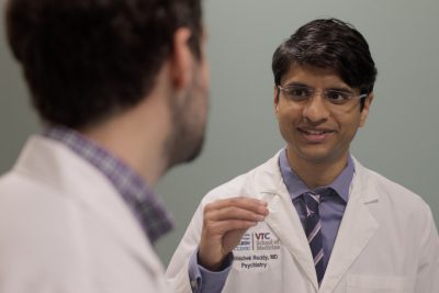 A doctor in a white medical coat gestures with his hand as he talks.