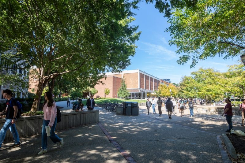 Hokies travel on paved pathways in front of Squires Student Center on a fall morning. Green trees frame the image. 